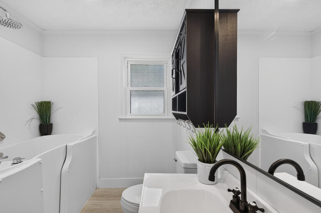 Bright bathroom with a white tub, vanity sink, dark cabinet, and frosted window.