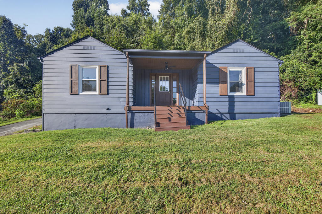 Gray single-story home with brown shutters and a covered porch above a sloping lawn.