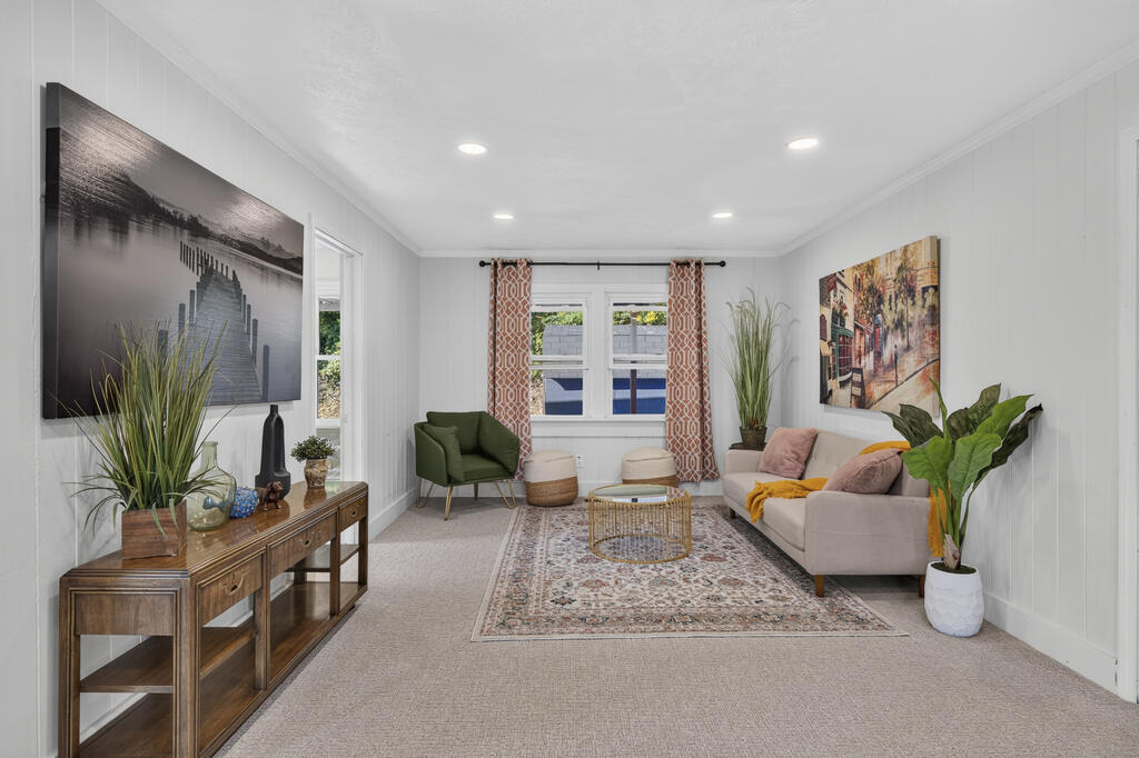 Staged living room with a beige sofa, green accent chair, patterned rug, and bright windows.
