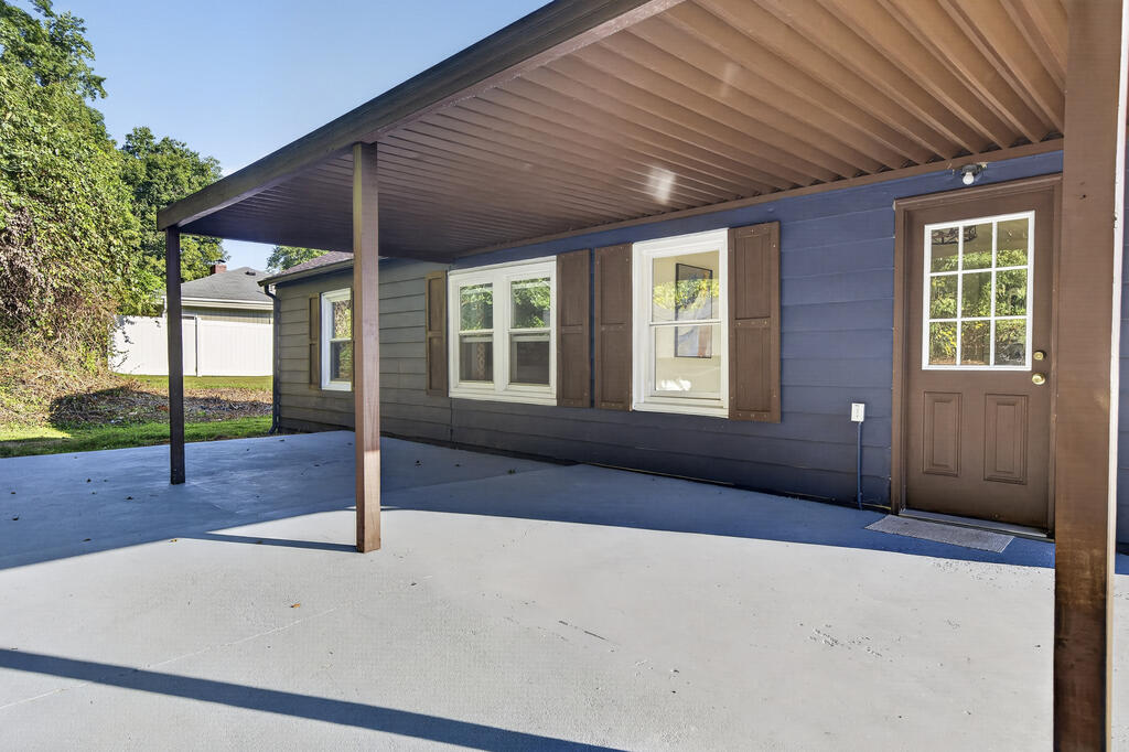 Covered concrete patio along a blue-sided home, with brown shutters and a glass-paneled door.