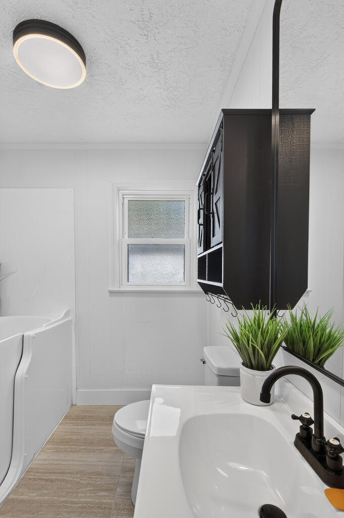 Bathroom with a white walk-in tub, dark wall cabinet, frosted window, and vanity with black faucet.