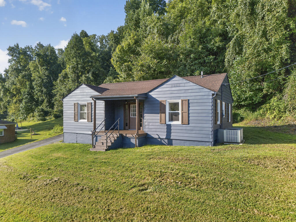 Blue-gray single-story house with brown shutters and a covered porch on a tree-lined lawn.