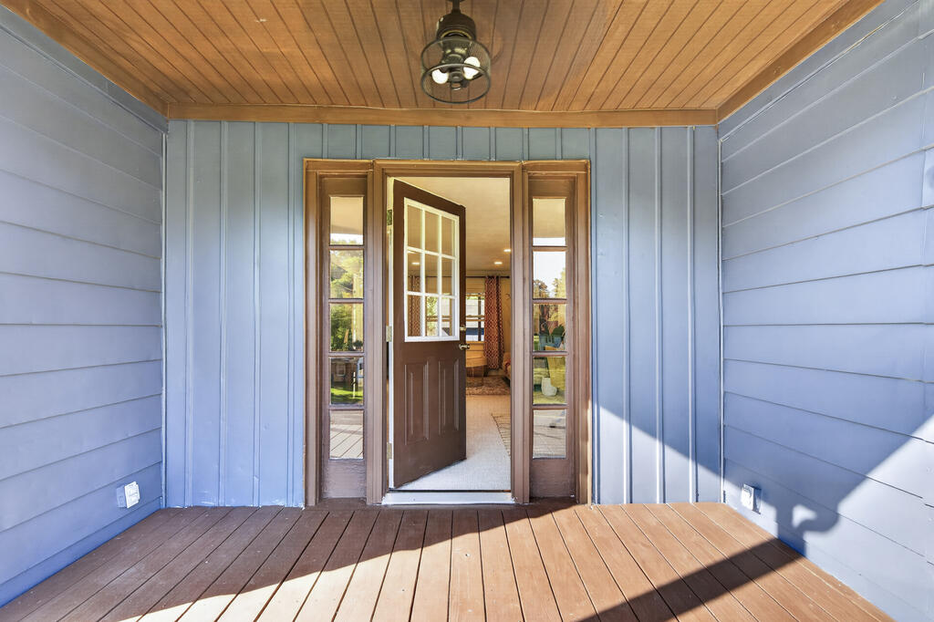 Covered wooden porch with blue siding and an open front door with sidelights.