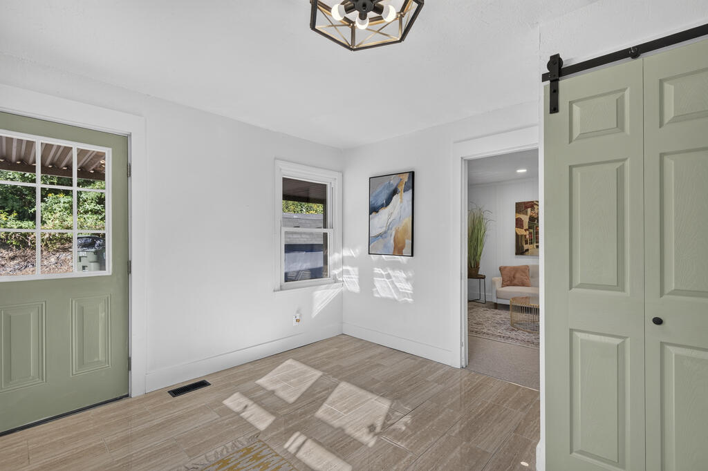Bright entryway with pale green doors, wood-look tile flooring, and a view into a sitting room.