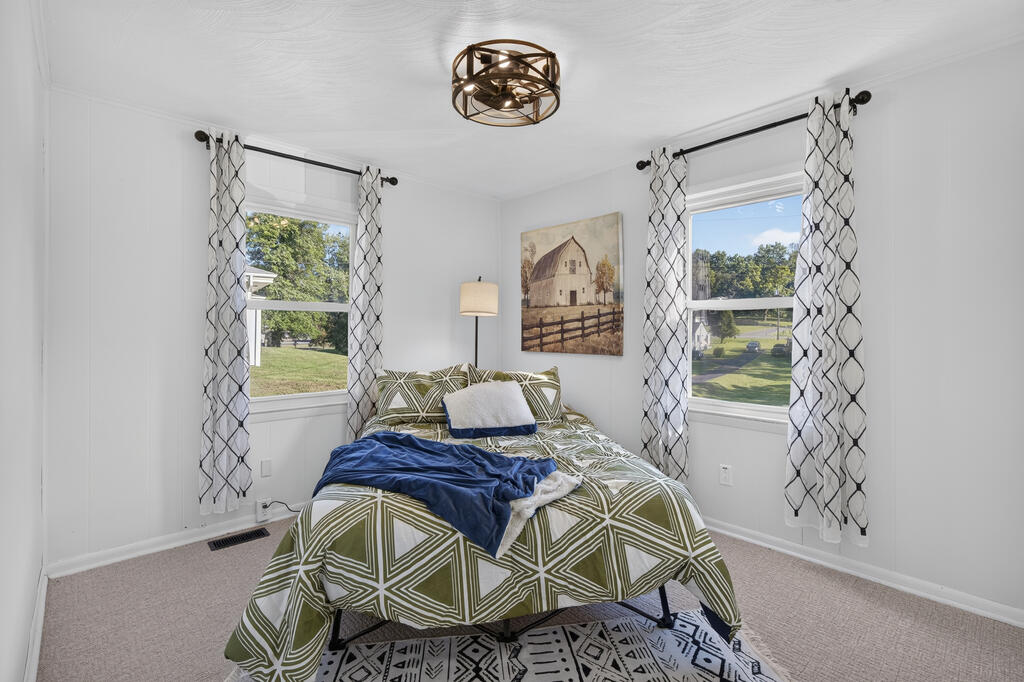 Bedroom with green geometric bedding, a blue throw, and two curtained windows.