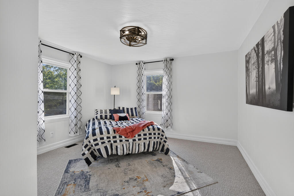 Bedroom with a black-and-white patterned bedspread, coral throw, and two curtained windows.