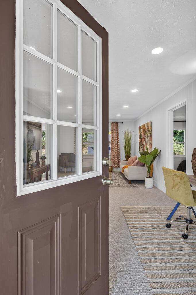 Furnished living room seen through an open glass-paneled door, with a white sofa and striped rug.