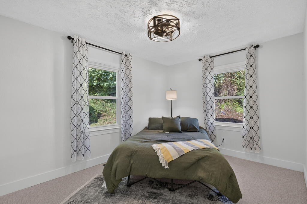 Bedroom with an olive-green bedspread, patterned throw, and two curtained windows.