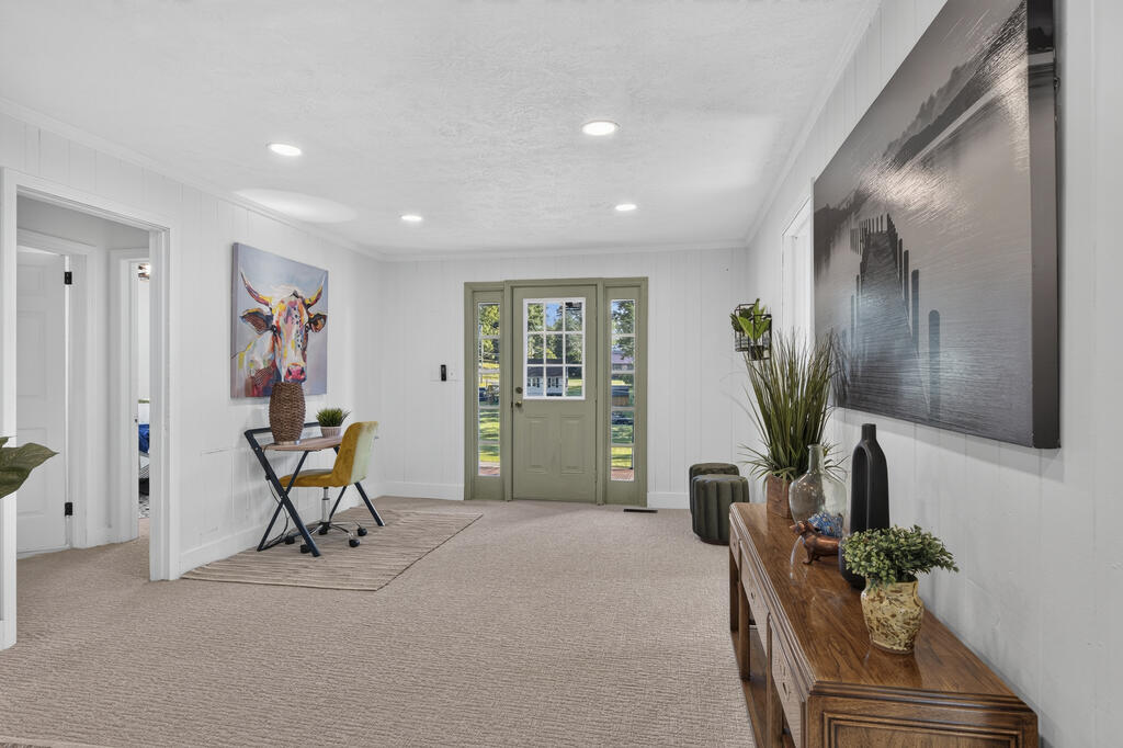Bright entry foyer with sage-green double doors, carpet, console table, and colorful cow artwork.