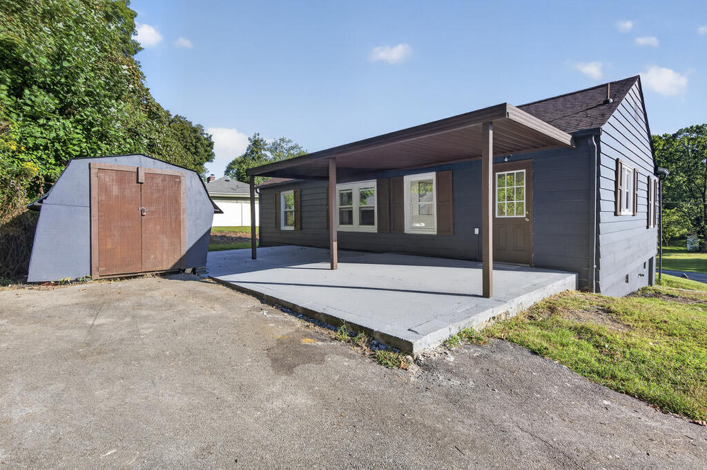 Dark-sided house with a covered concrete patio and detached storage shed.