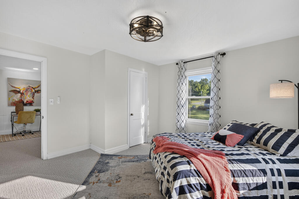 Staged bedroom with navy-and-white striped bedding, coral throws, and a window overlooking greenery.