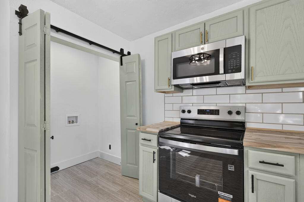 Kitchen with sage-green cabinets, butcher-block counters, subway tile, and stainless steel appliances.