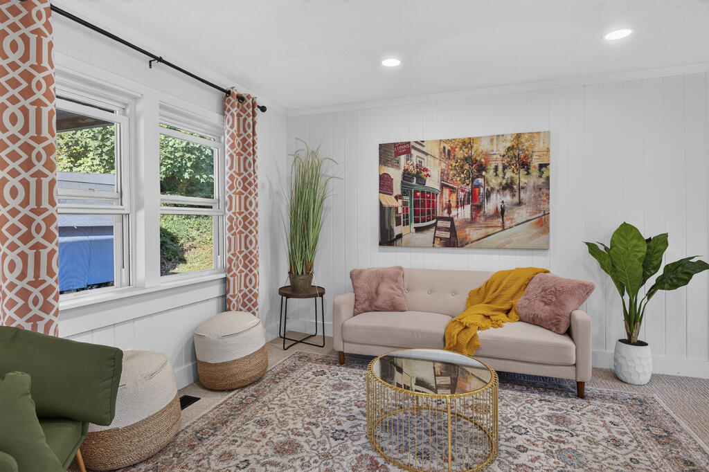 Staged living room with a blush sofa, mustard throw, gold coffee table, and large curtained windows.