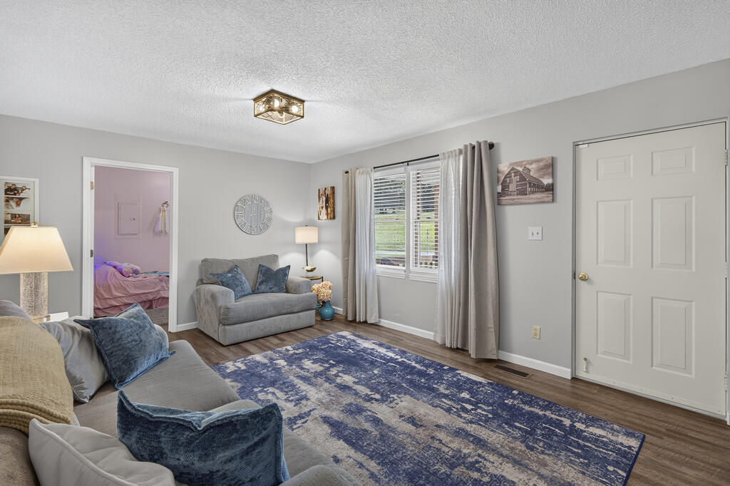 Furnished living room with gray sofas, a blue patterned rug, and an open doorway to a bedroom.