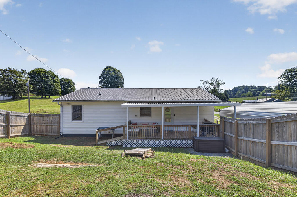Rear of a white single-story house with a covered porch, wooden ramp, and fenced grassy yard.