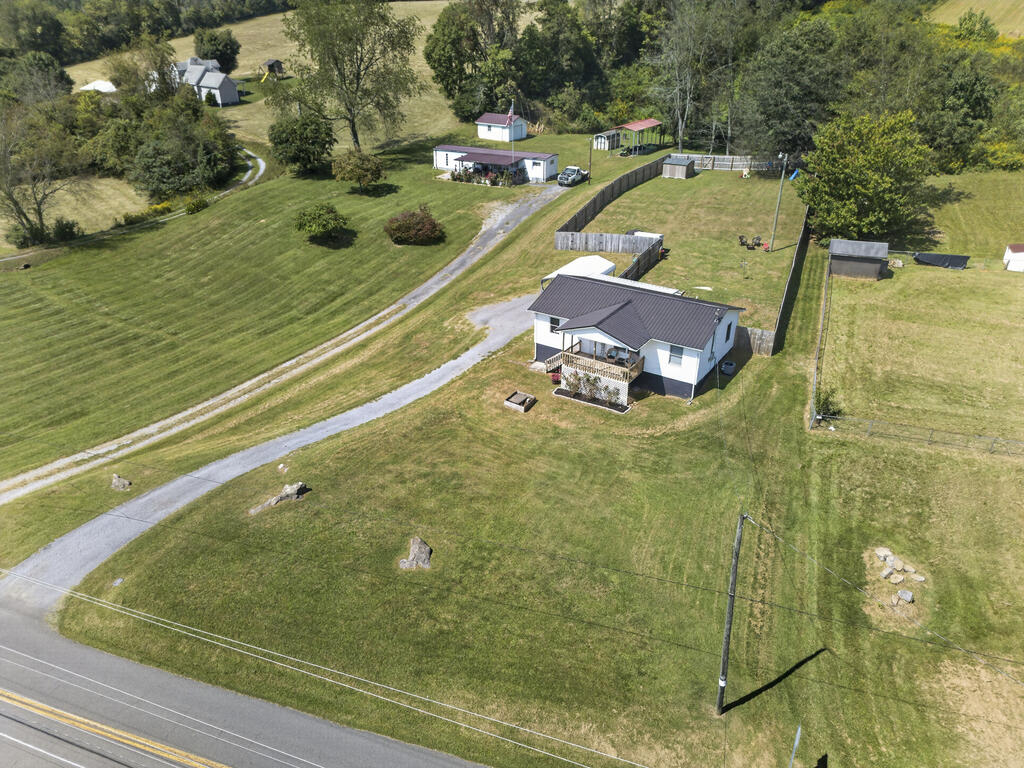 Aerial view of a white home with a dark roof, fenced yard, gravel drive, and outbuildings.