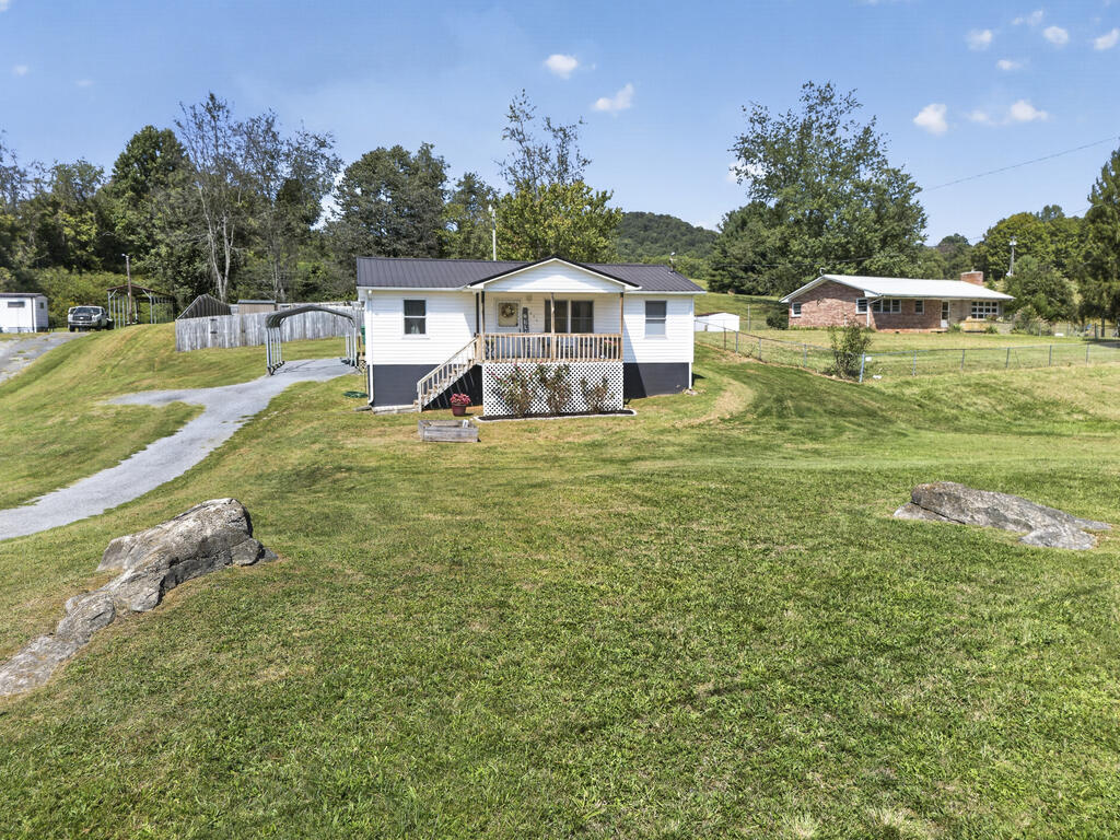 White single-story house with a covered porch on a broad grassy lot beside a curved driveway.