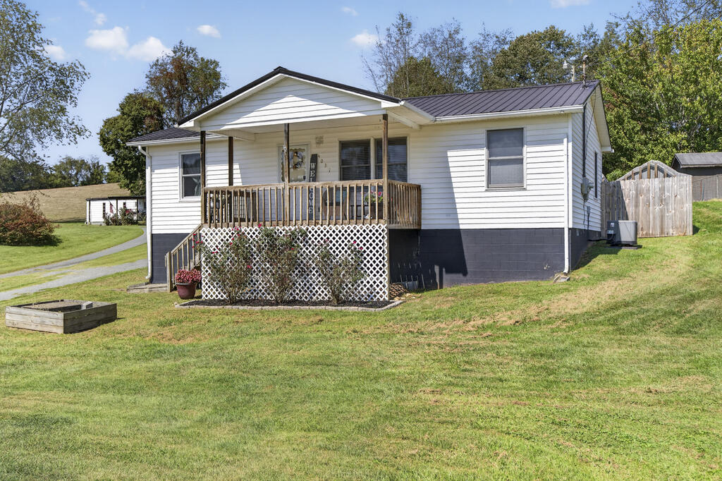 White single-story home with a covered front porch, wooden railings, and a broad lawn.