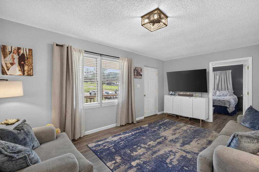 Living room with gray sofas, a blue patterned rug, and a television beside an open bedroom doorway.