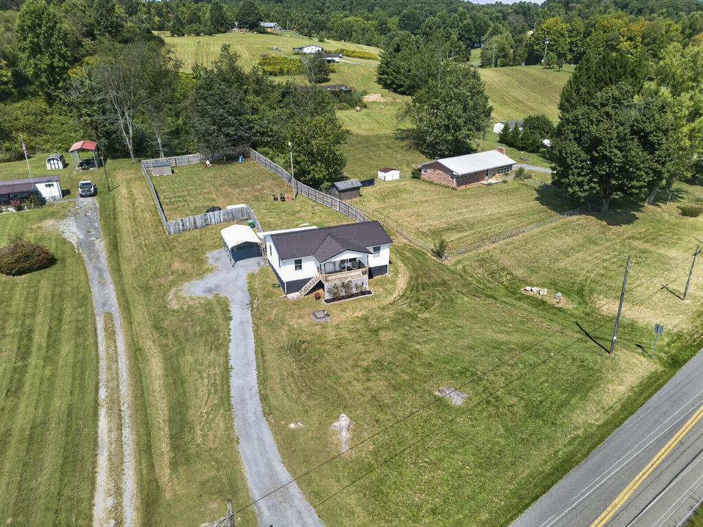 Aerial view of a white house with a fenced yard, gravel driveway, and open grassy grounds.
