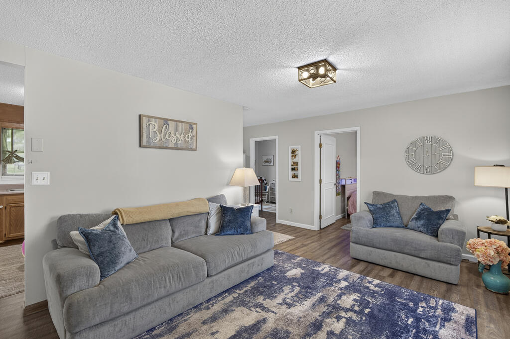 Living room with two gray sofas, blue pillows, a patterned rug, and a large wall clock.