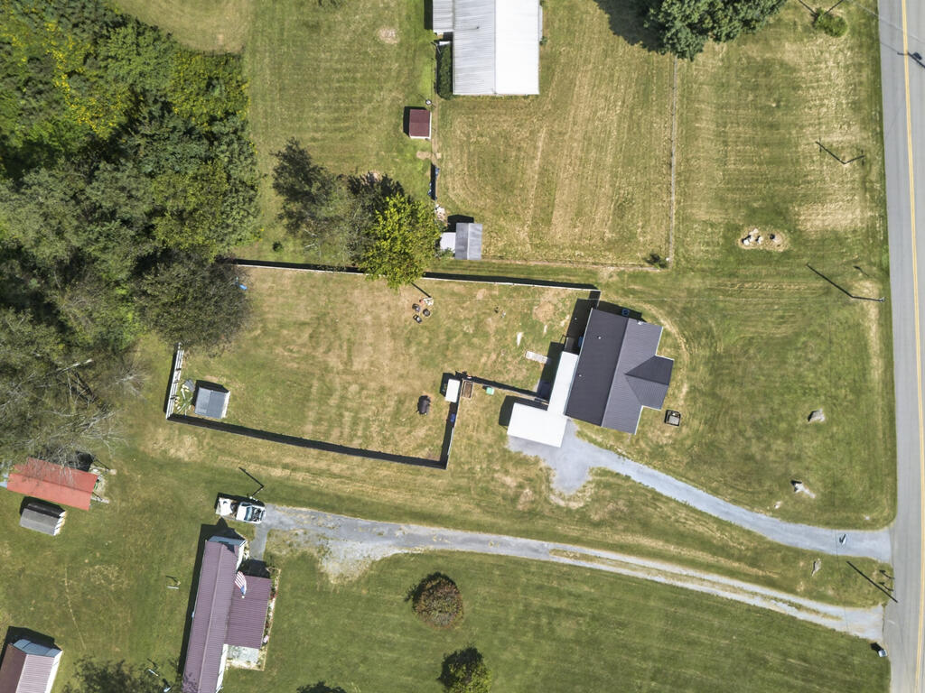 Aerial view of a house and fenced yard beside a road, with a gravel driveway.