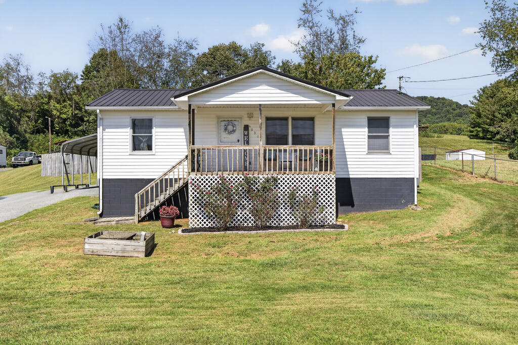 White single-story house with a covered porch, lattice skirting, dark metal roof, and broad front lawn.