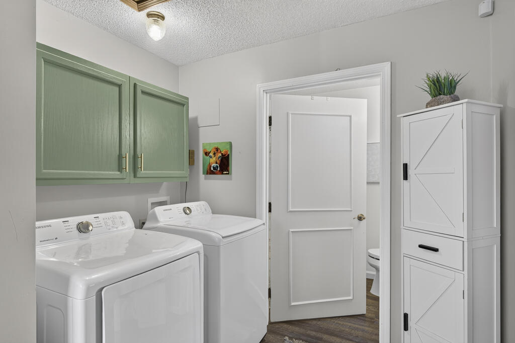 Laundry room with a washer and dryer, sage-green cabinets, and an adjoining bathroom.