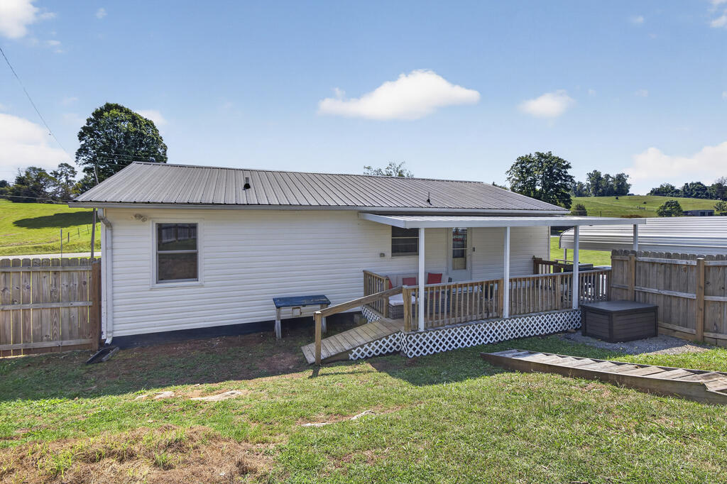 White single-story home with a metal roof, covered porch, and wooden ramp in a fenced yard.