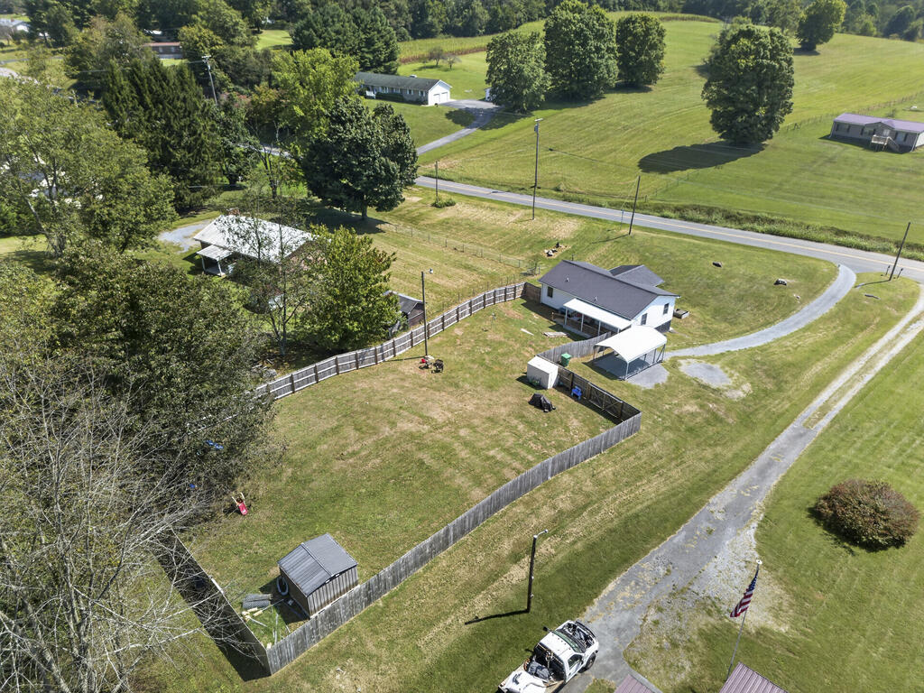Aerial view of a white house and fenced yard with outbuildings and a curving driveway.