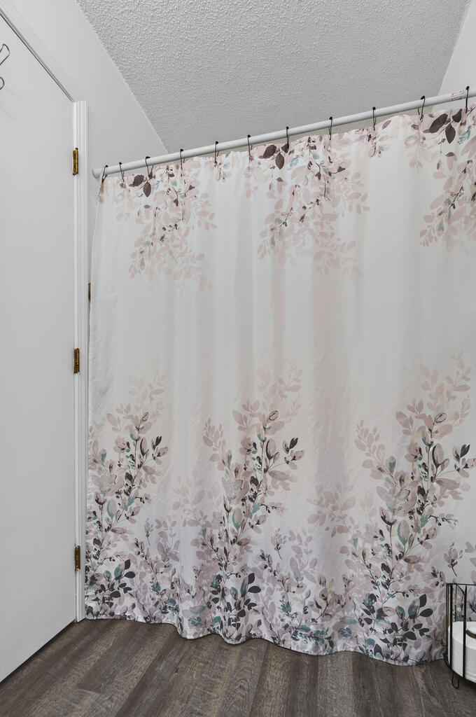 Bathroom with a floral shower curtain and dark wood-look flooring.