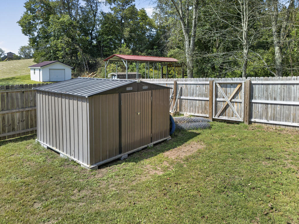 Fenced yard with a large brown metal shed, a smaller hillside shed, and a red-roofed shelter.