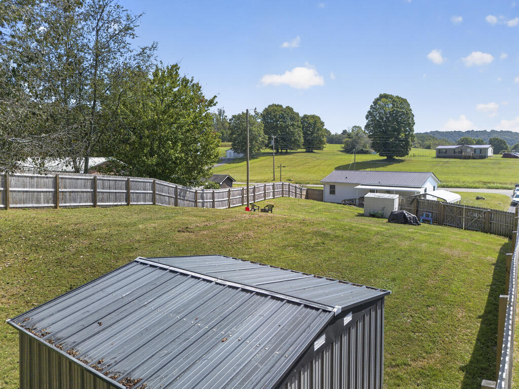 Fenced grassy yard with a metal-roofed shed, outbuildings, and open countryside beyond.