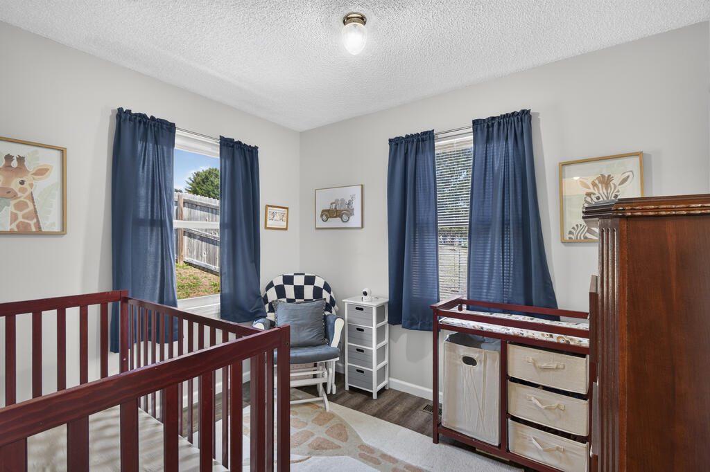 Nursery with two dark wood cribs, a changing table, and a rocking chair by blue-curtained windows.