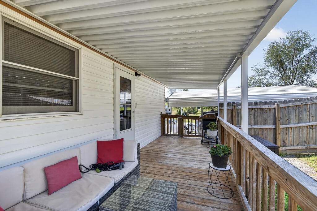 Covered wooden deck with a cushioned sofa, glass-top table, and potted plants.