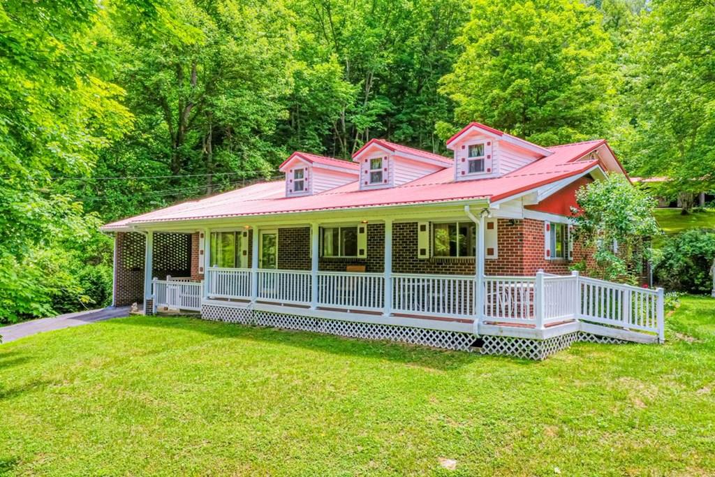 Brick house with a red metal roof and long white-railed porch, surrounded by trees.