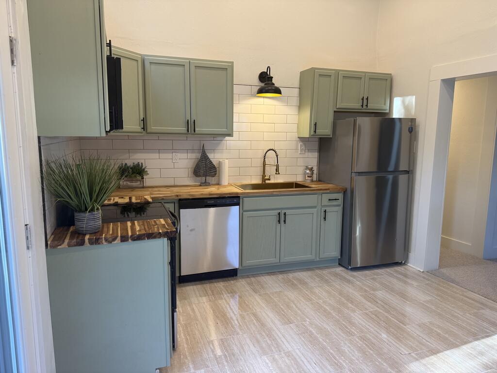 Kitchen with sage green cabinets, butcher-block counters, and stainless steel appliances.