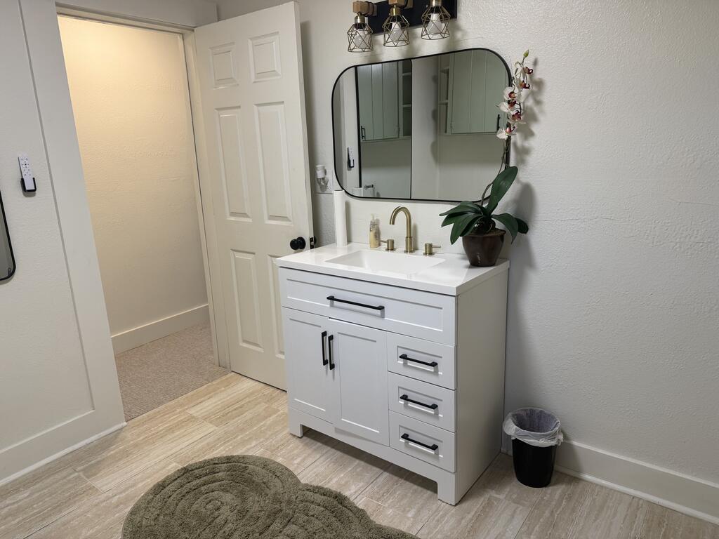 Bathroom with a white vanity, brass faucet, rounded mirror, and potted orchid.