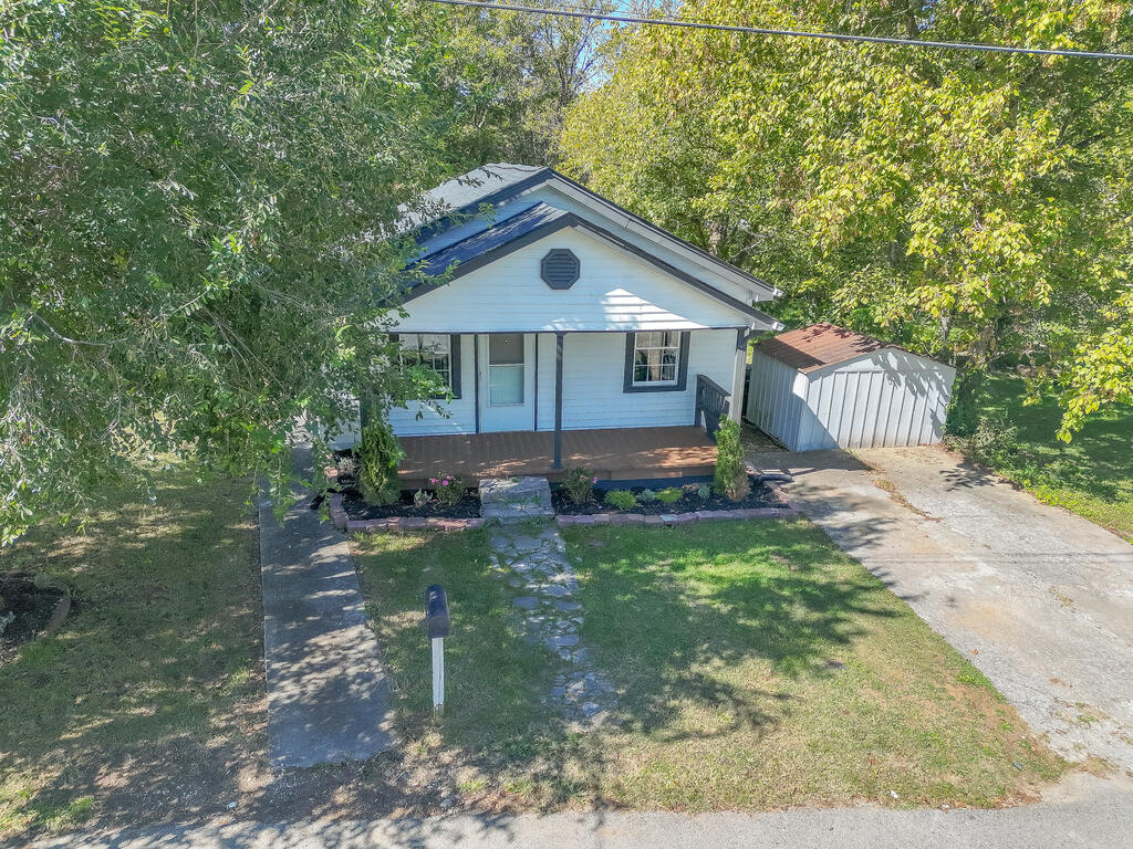 Light-blue house with a covered porch, detached shed, and stone walkway, viewed from above.