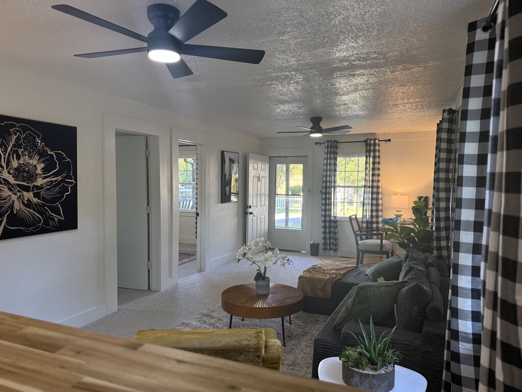Furnished living room with two ceiling fans, checkered curtains, and a glass door to the porch.