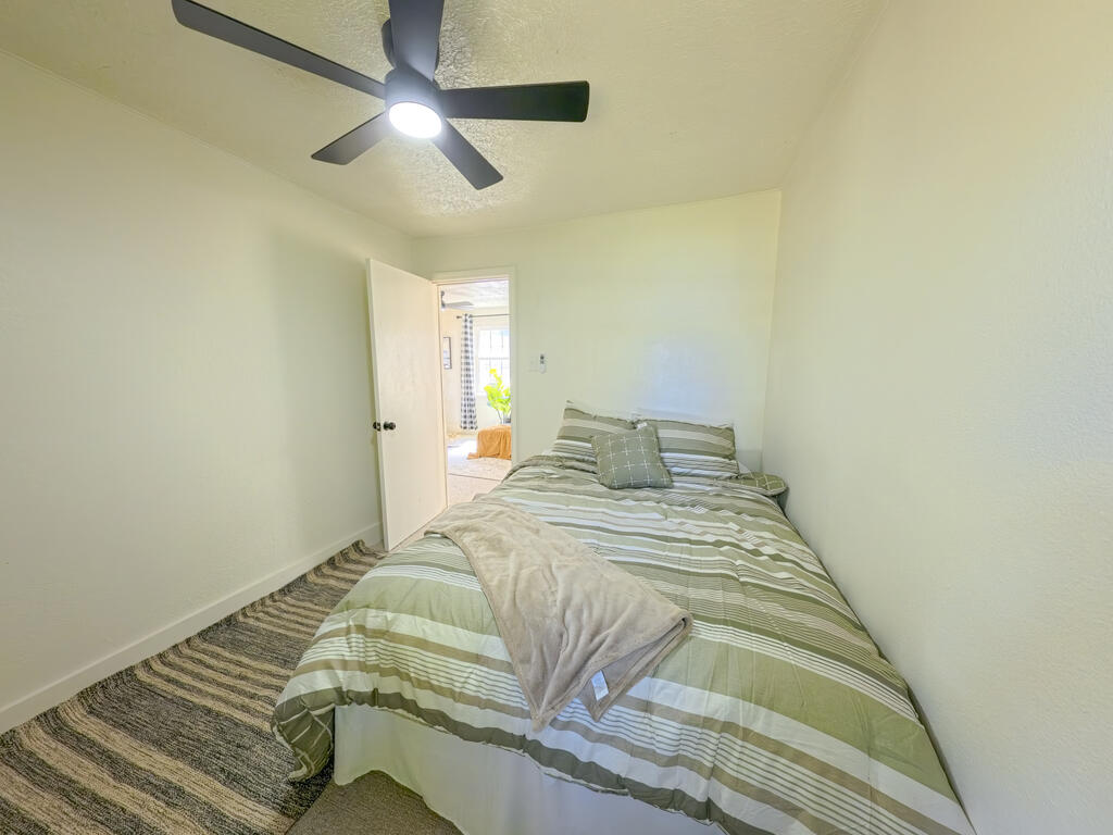 Bedroom with green-and-white striped bedding and a ceiling fan.