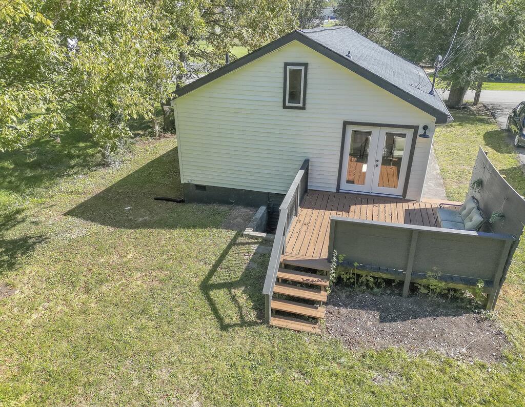 Rear of a white-sided house with a raised wooden deck and steps overlooking a grassy yard.