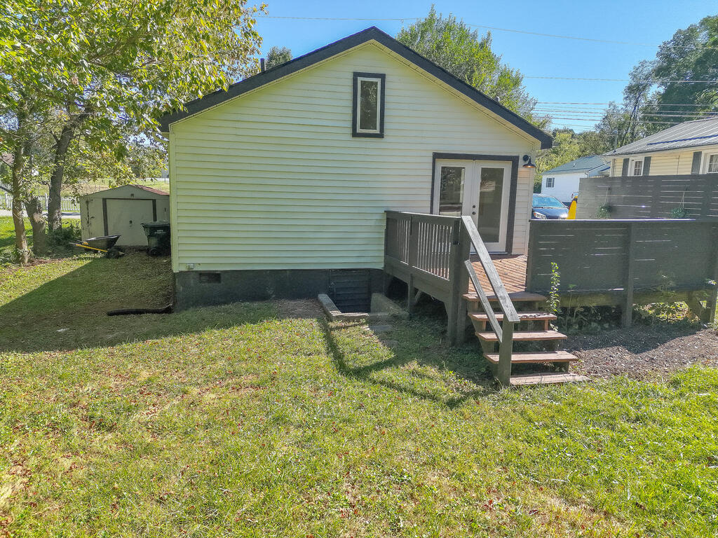 Rear of a light-colored house with a raised deck and stairs opening onto a grassy yard.