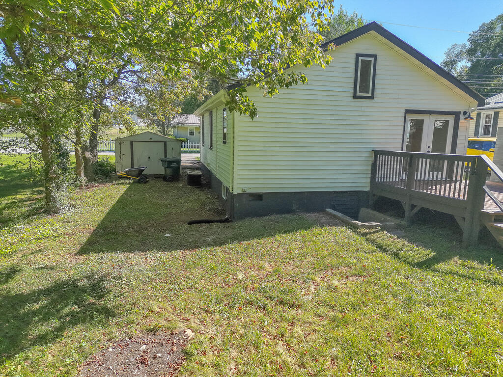 Rear of a light-colored house with a raised deck, a small shed, and a shady grassy yard.
