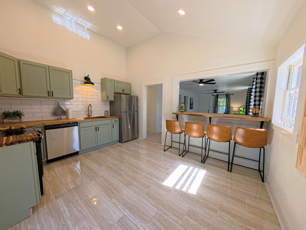 Kitchen with sage-green cabinets, stainless appliances, and a breakfast bar opening to the living room.
