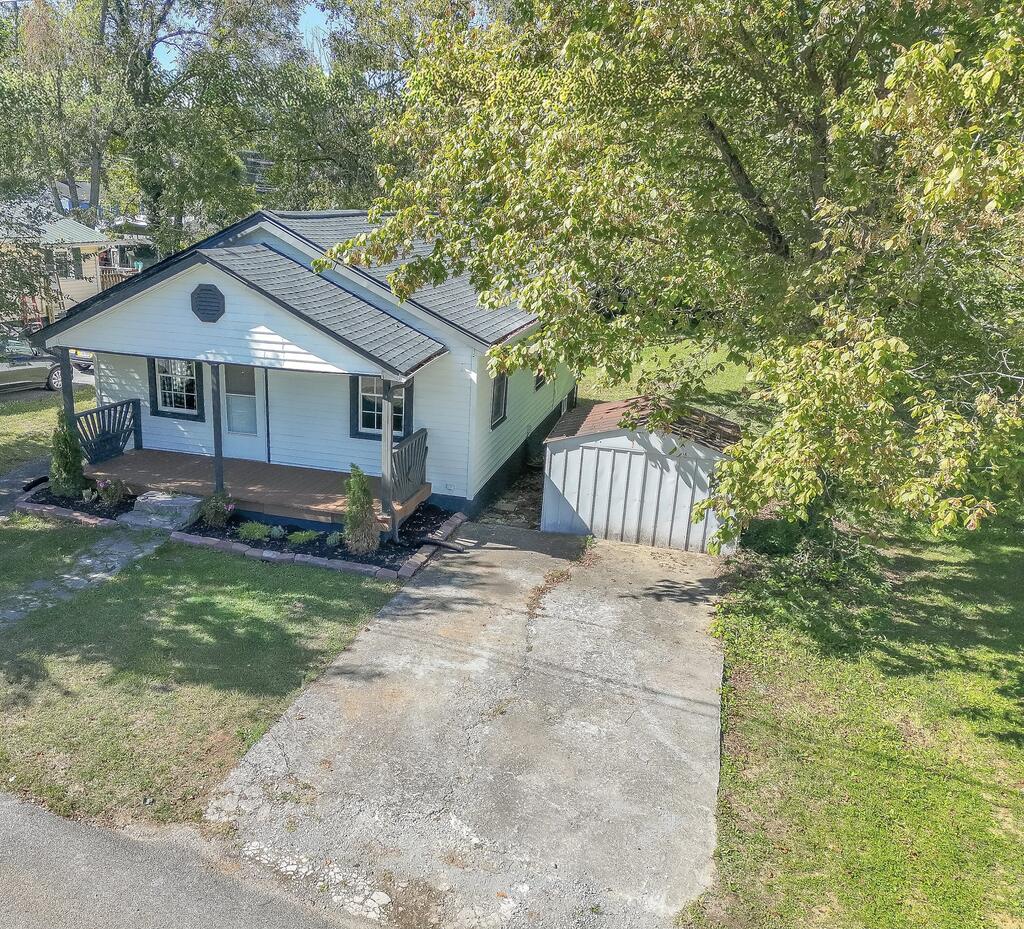 White single-story house with a covered porch, concrete driveway, and detached shed, viewed from above.