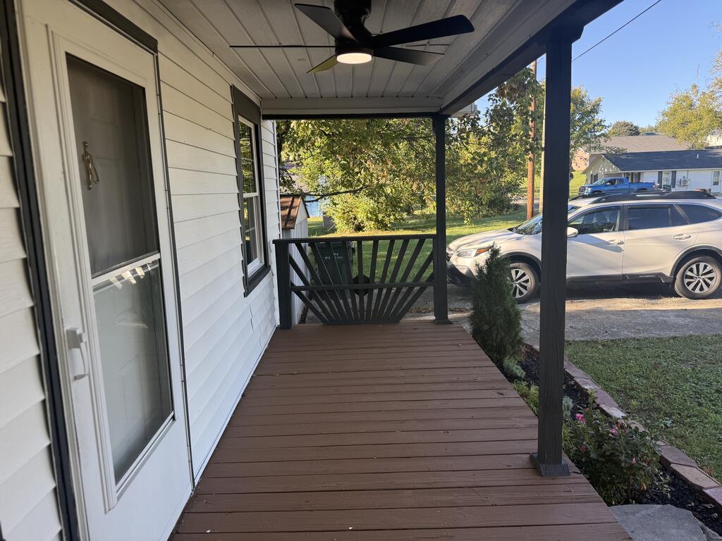 Covered front porch with brown decking, black railing, and ceiling fan.