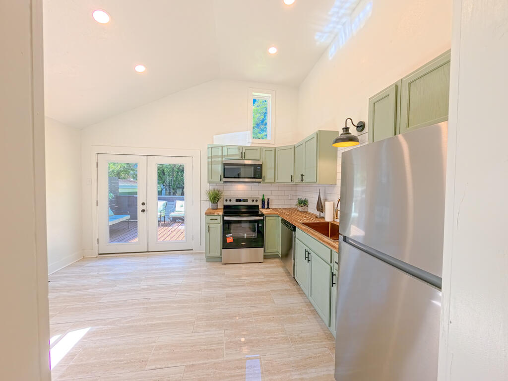 Kitchen with pale green cabinets, stainless steel appliances, wood counters, and French doors to a deck.