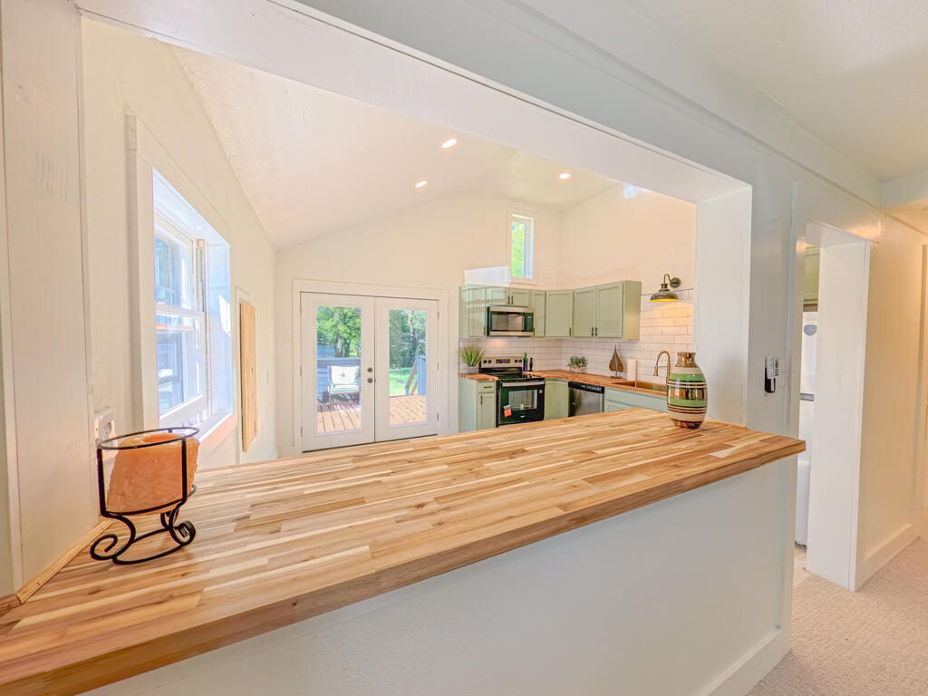 Kitchen with sage-green cabinets and a long butcher-block peninsula overlooking glass doors to a sunny deck.