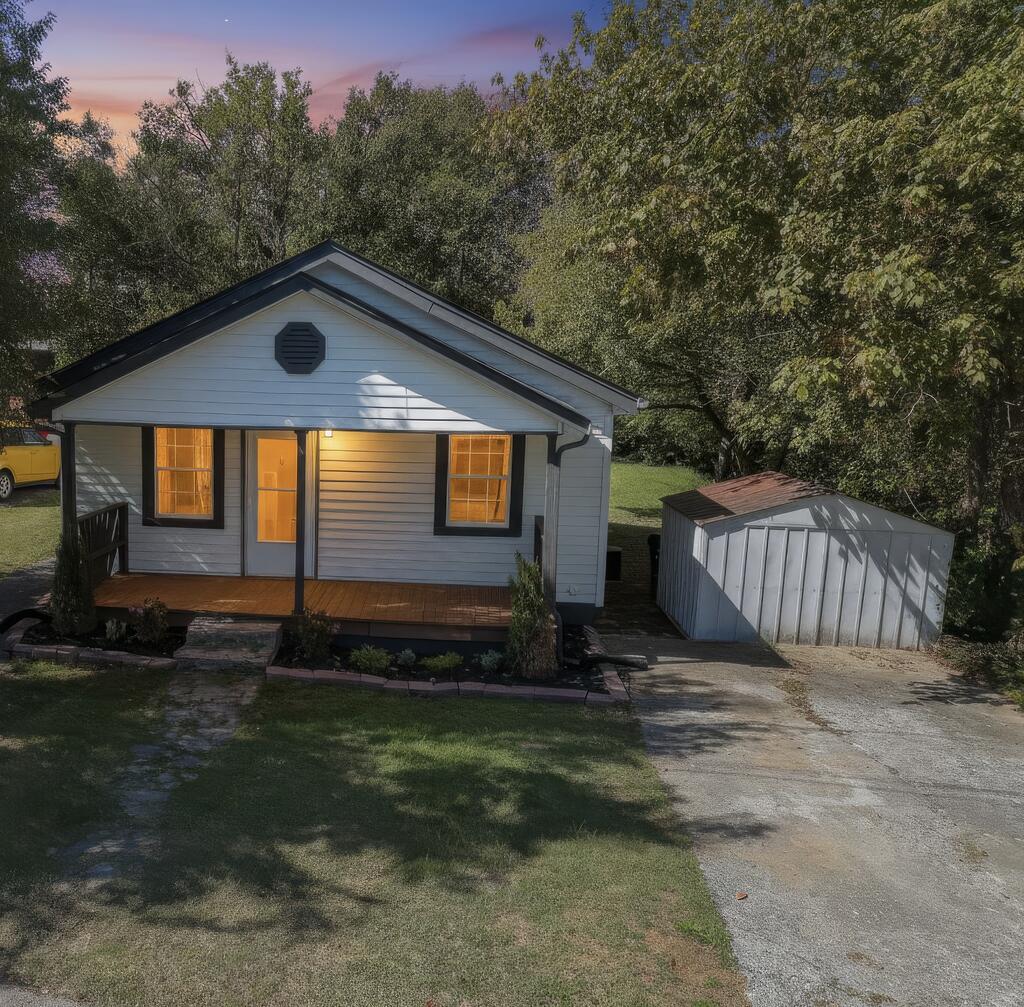 Gray single-story house with a covered porch, glowing windows, and a detached storage shed.